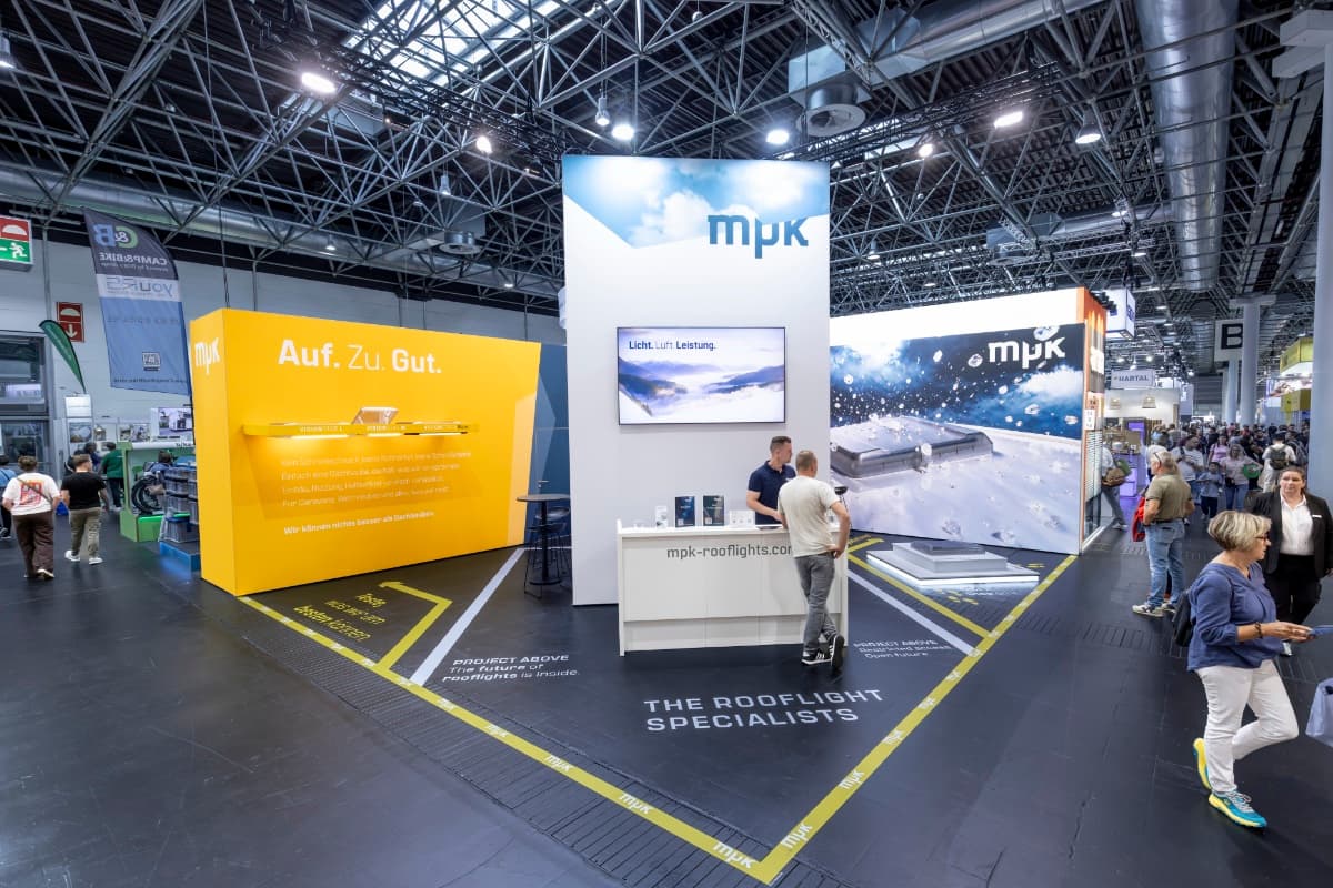 MPK Messestand auf dem Caravan Salon: gelbe Wand Auf. Zu. Gut., weißer Turm mit mpk-Logo, Hagelwand und Bodentypografie THE ROOFLIGHT SPECIALISTS