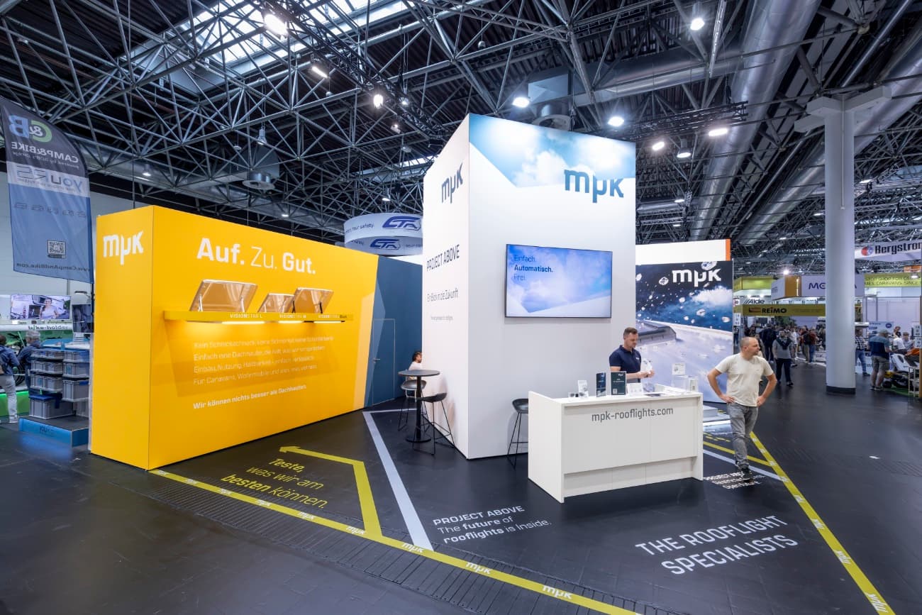 MPK Messestand mit dem hohen Project-Above-Kubus, Personen davor zeigen die Dimension des Wuerfels