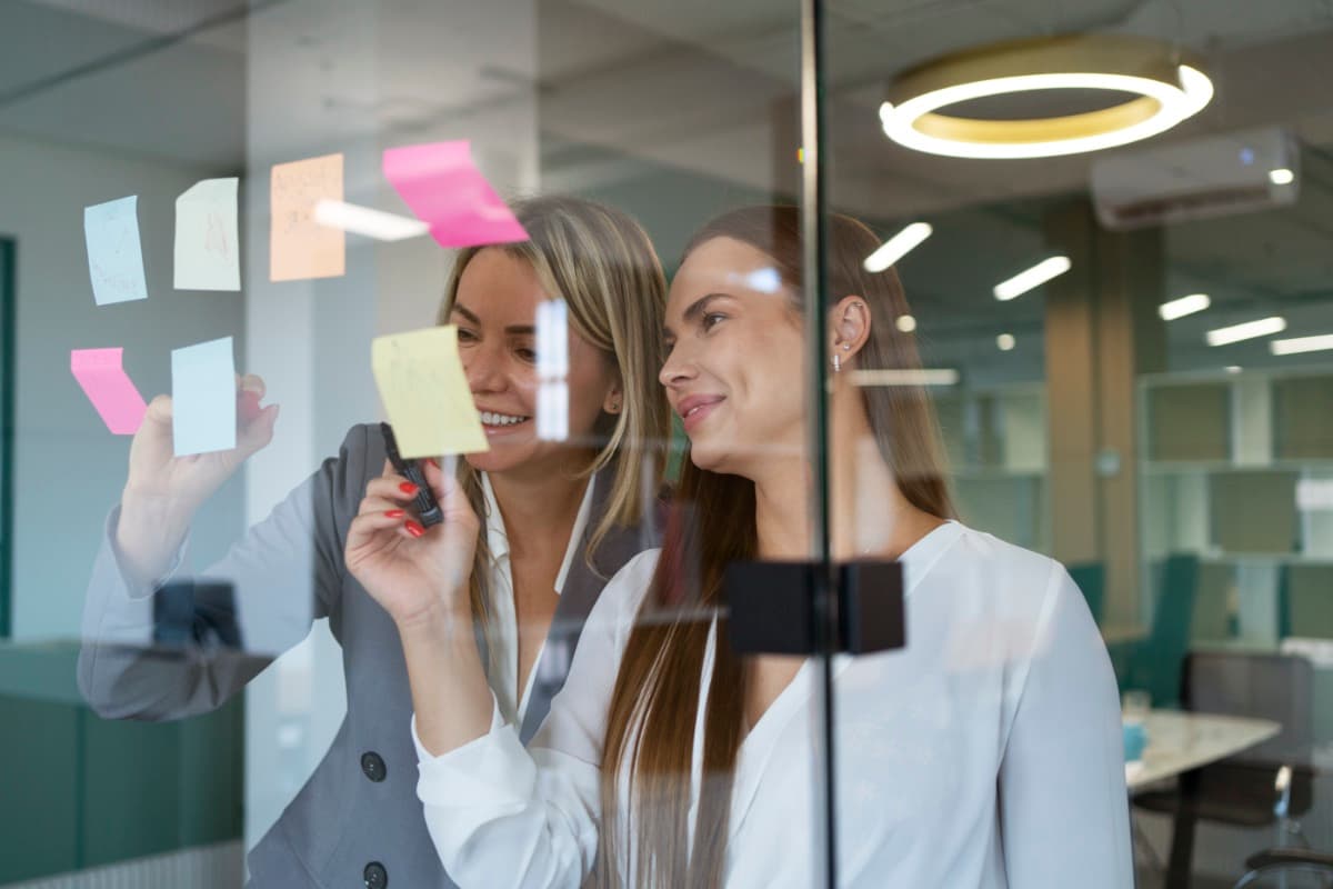 Zwei Kolleginnen arbeiten an einer Glaswand mit Post-its an einer Strategie