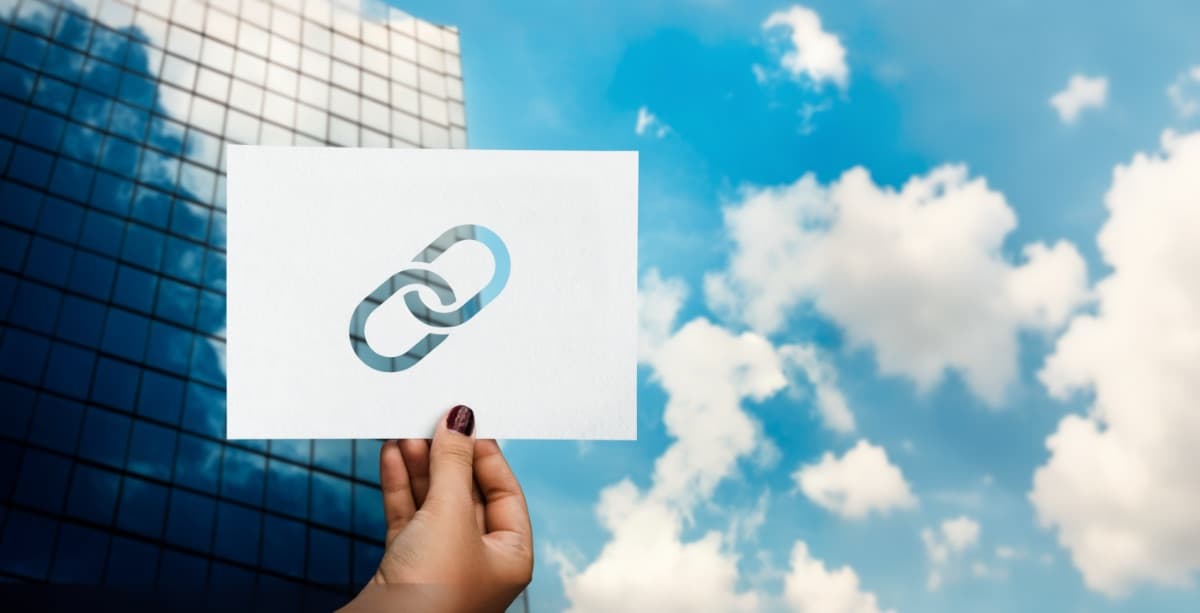 Hand hält Papier mit Ketten-Symbol vor blauem Himmel als Symbol für Content Marketing und Verbindung