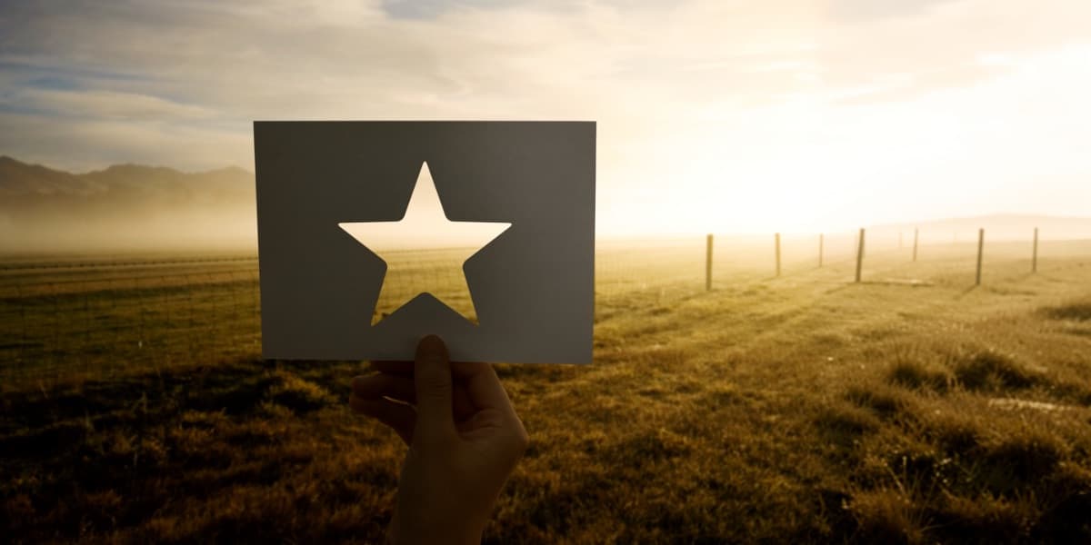 Hand hält Karte mit Stern-Ausschnitt vor goldenem Sonnenaufgang als Symbol für SEO-Sichtbarkeit und Exzellenz